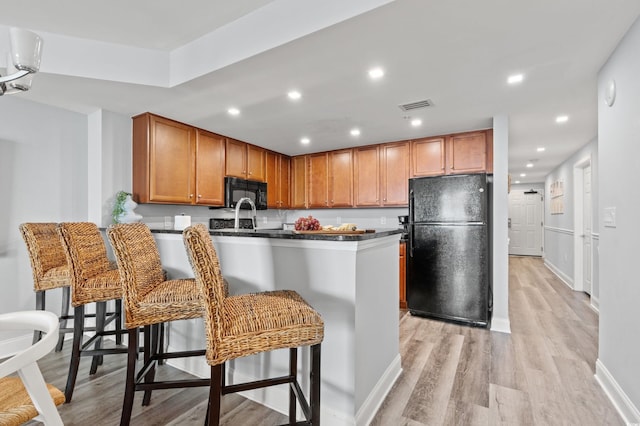 kitchen with black appliances, a breakfast bar, kitchen peninsula, and light hardwood / wood-style flooring