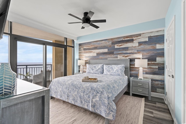 bedroom with access to exterior, ceiling fan, dark hardwood / wood-style flooring, wooden walls, and a water view