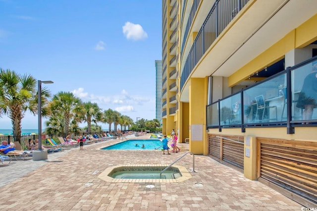 view of pool featuring a patio area, a water view, and a hot tub