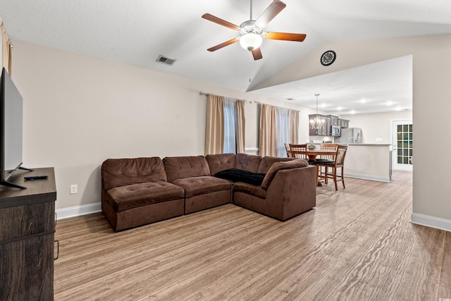 living room featuring ceiling fan with notable chandelier, light hardwood / wood-style flooring, and vaulted ceiling