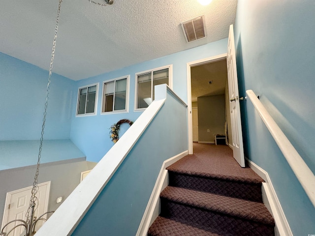 staircase featuring carpet flooring, a textured ceiling, and lofted ceiling