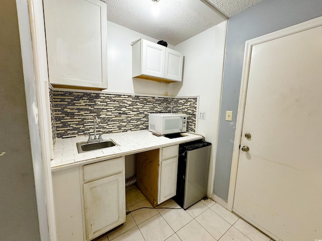 kitchen with sink, backsplash, tile countertops, a textured ceiling, and light tile patterned floors