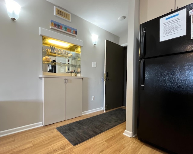 interior space featuring white cabinetry, light hardwood / wood-style floors, and black fridge