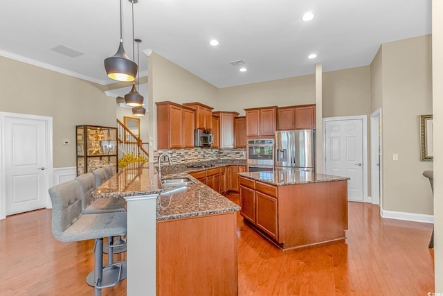 kitchen featuring kitchen peninsula, hanging light fixtures, appliances with stainless steel finishes, light hardwood / wood-style floors, and sink