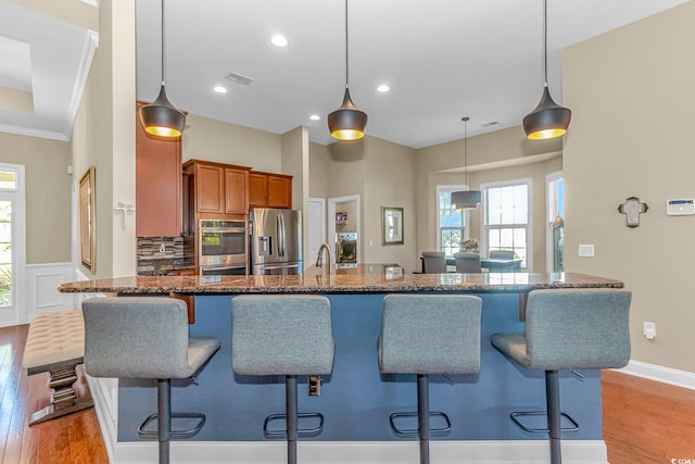 kitchen featuring light wood-type flooring, a kitchen breakfast bar, hanging light fixtures, stainless steel appliances, and crown molding