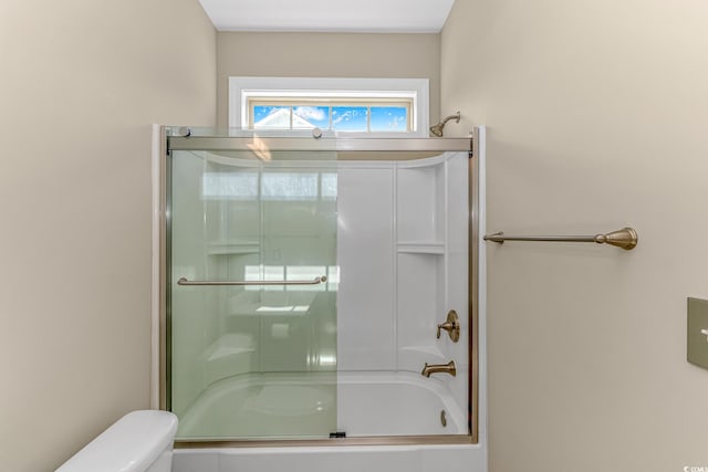 bathroom featuring toilet and bath / shower combo with glass door