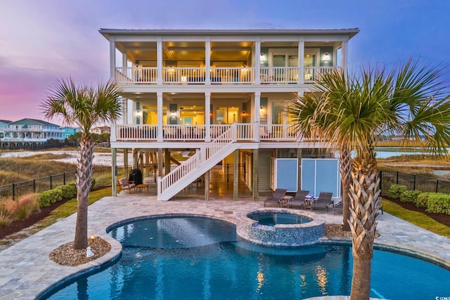 back house at dusk with a patio area, a swimming pool with hot tub, and a balcony