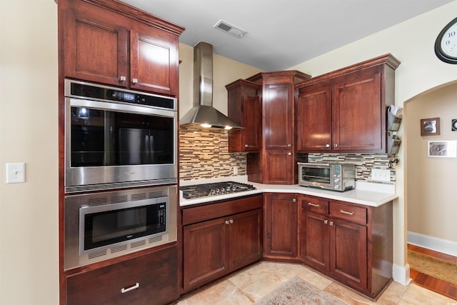 kitchen with wall chimney range hood, backsplash, light tile patterned flooring, and stainless steel appliances