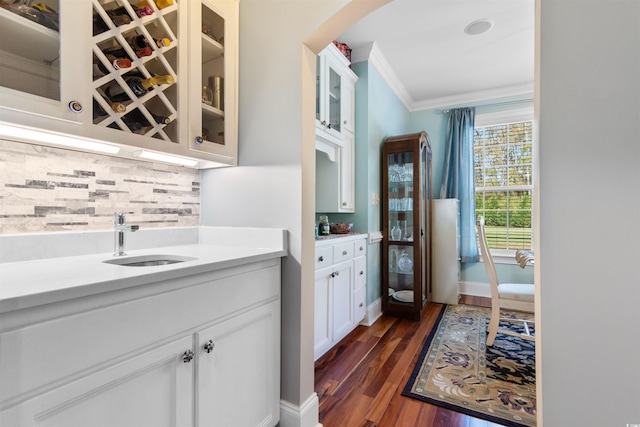 kitchen with dark wood-type flooring, white cabinets, sink, crown molding, and backsplash