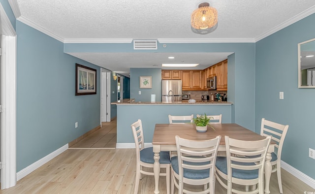 dining room featuring a textured ceiling, light hardwood / wood-style flooring, and ornamental molding