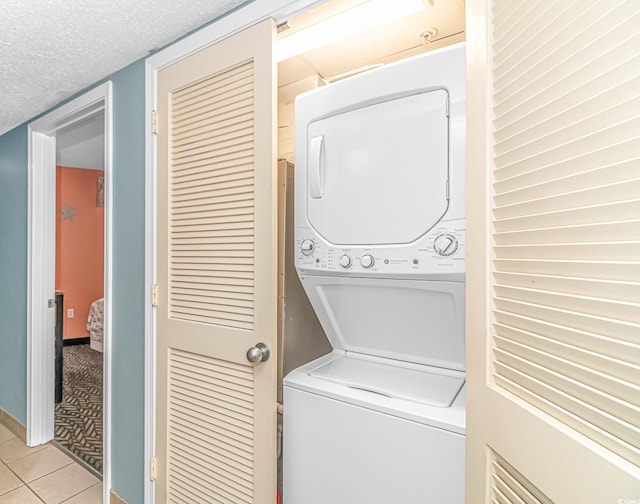 laundry room featuring stacked washer / dryer, light tile patterned flooring, and a textured ceiling