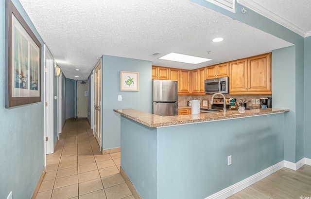 kitchen featuring stainless steel appliances, kitchen peninsula, a textured ceiling, light tile patterned floors, and ornamental molding