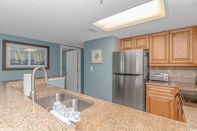 kitchen featuring a textured ceiling, stainless steel fridge, light stone counters, and sink