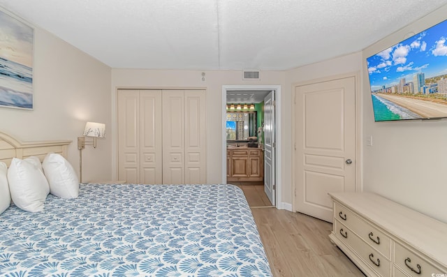 bedroom featuring ensuite bath, a closet, light hardwood / wood-style floors, and a textured ceiling