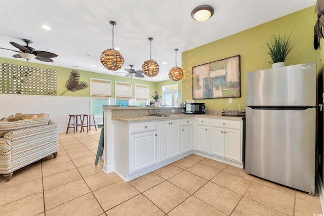 kitchen with stainless steel refrigerator, white cabinetry, sink, pendant lighting, and light tile patterned floors