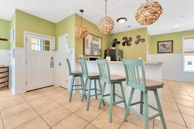 kitchen featuring a kitchen bar, stainless steel refrigerator, light tile patterned floors, and pendant lighting