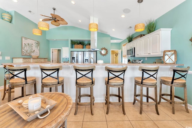 kitchen with appliances with stainless steel finishes, a kitchen breakfast bar, vaulted ceiling, ceiling fan, and white cabinetry