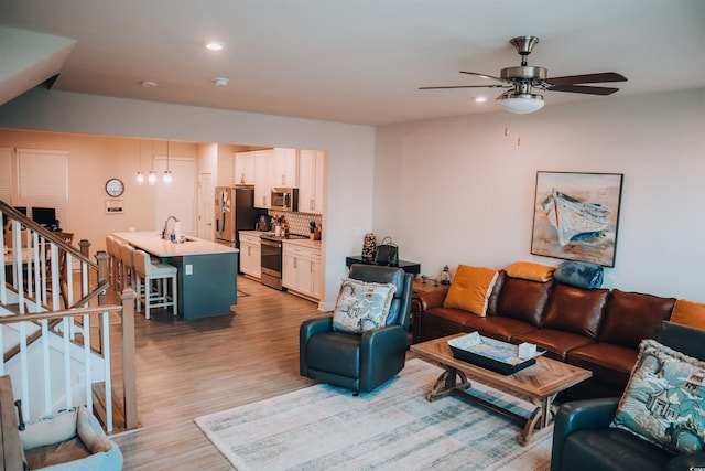 living room featuring light wood-type flooring, sink, and ceiling fan