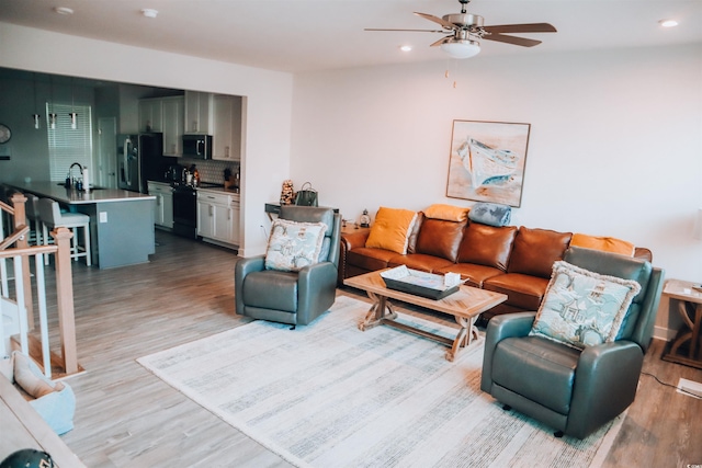 living room featuring light hardwood / wood-style flooring, lofted ceiling, sink, and ceiling fan