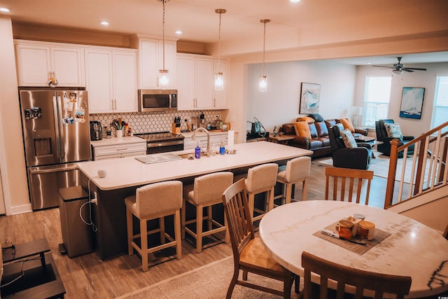 kitchen with a center island with sink, stainless steel appliances, white cabinetry, hanging light fixtures, and ceiling fan