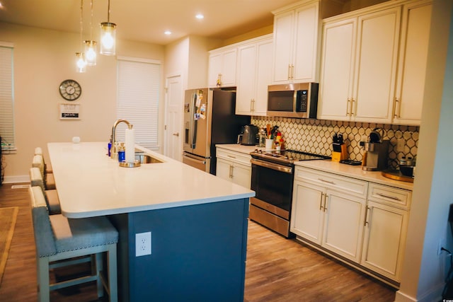 kitchen with light wood-type flooring, sink, a kitchen island with sink, and appliances with stainless steel finishes