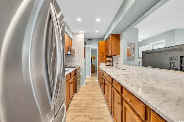 kitchen with backsplash, appliances with stainless steel finishes, light stone countertops, and light hardwood / wood-style floors