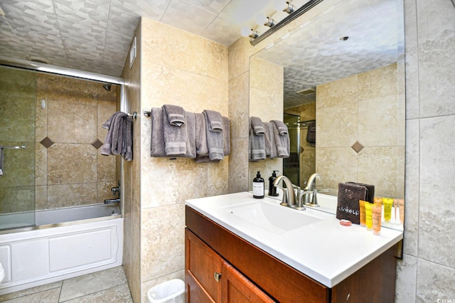 bathroom with tile patterned floors, vanity, bath / shower combo with glass door, and tile walls