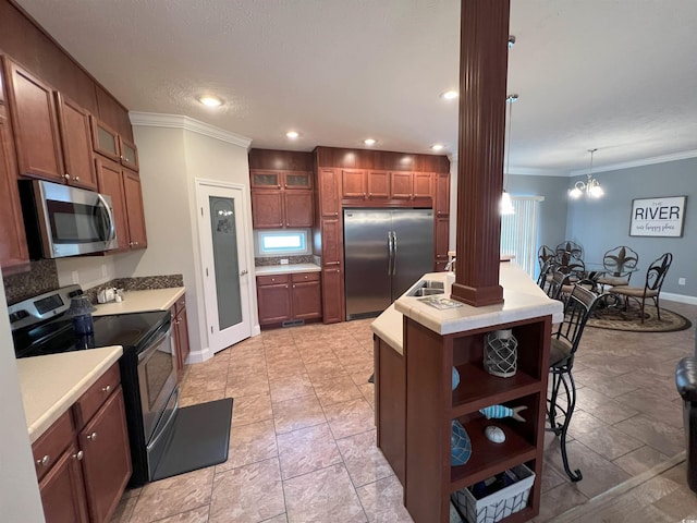 kitchen with stainless steel appliances, a notable chandelier, an island with sink, ornamental molding, and decorative light fixtures