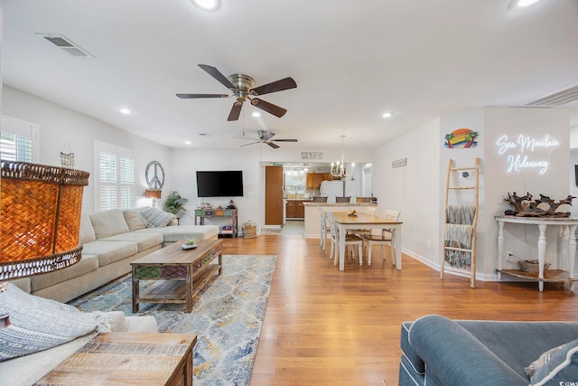 living room featuring ceiling fan with notable chandelier and light wood-type flooring