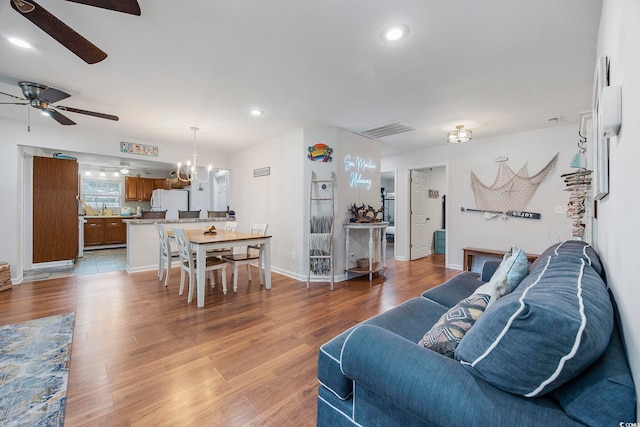 living room with ceiling fan with notable chandelier and light hardwood / wood-style flooring