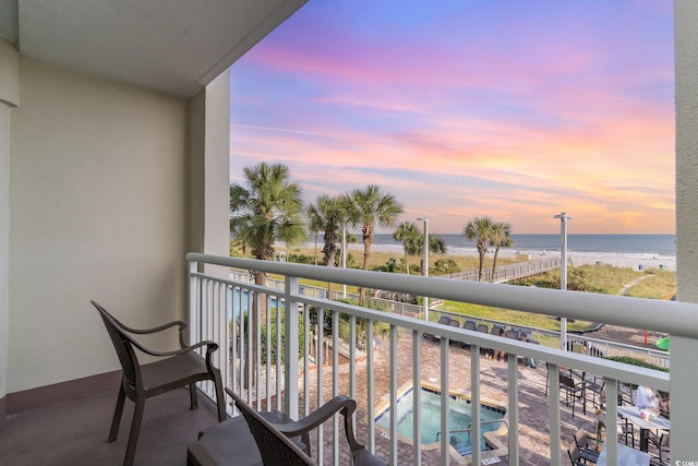 balcony at dusk featuring a water view and an in ground hot tub