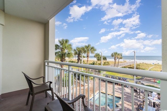 balcony featuring a beach view, a water view, and an in ground hot tub