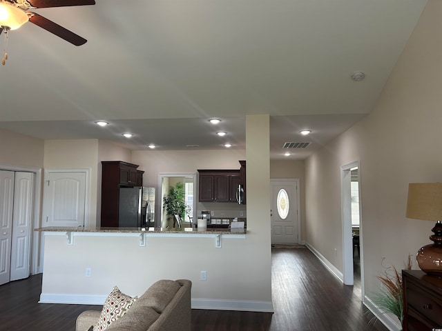 kitchen with stainless steel appliances, light stone counters, kitchen peninsula, a kitchen bar, and dark hardwood / wood-style floors