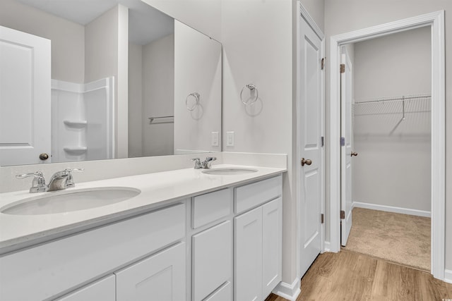full bath featuring a sink, double vanity, wood finished floors, and a spacious closet