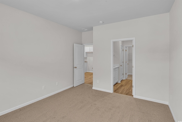 unfurnished bedroom featuring baseboards, connected bathroom, visible vents, and light carpet
