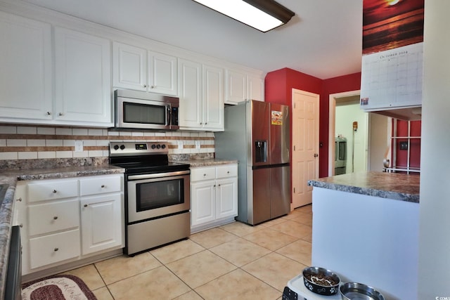 kitchen featuring decorative backsplash, stainless steel appliances, white cabinets, washer / dryer, and light tile patterned flooring