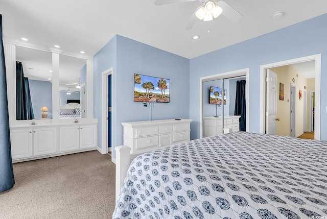 bedroom with ceiling fan, ensuite bathroom, light colored carpet, and a closet