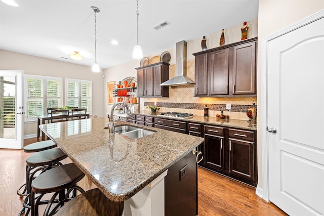 kitchen with an island with sink, sink, wall chimney exhaust hood, and a kitchen breakfast bar