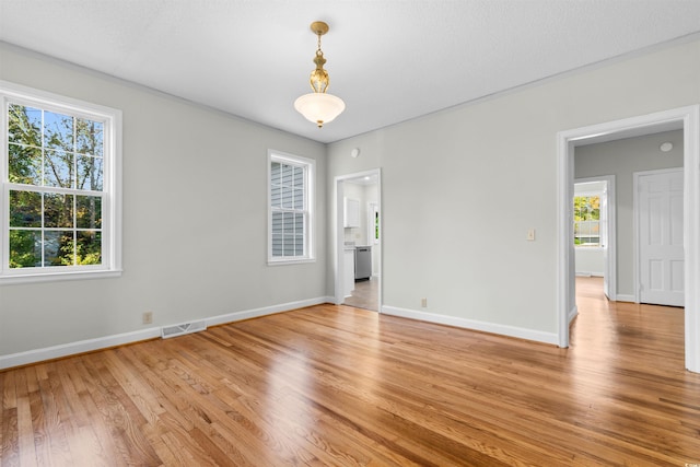 empty room featuring baseboards, light wood-type flooring, visible vents, and a healthy amount of sunlight