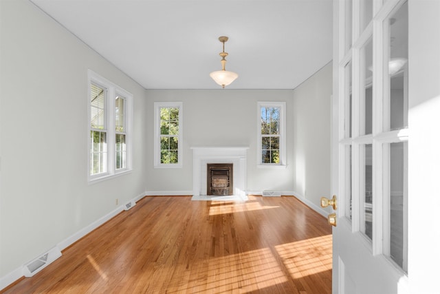 unfurnished living room featuring baseboards, a fireplace with flush hearth, visible vents, and wood finished floors