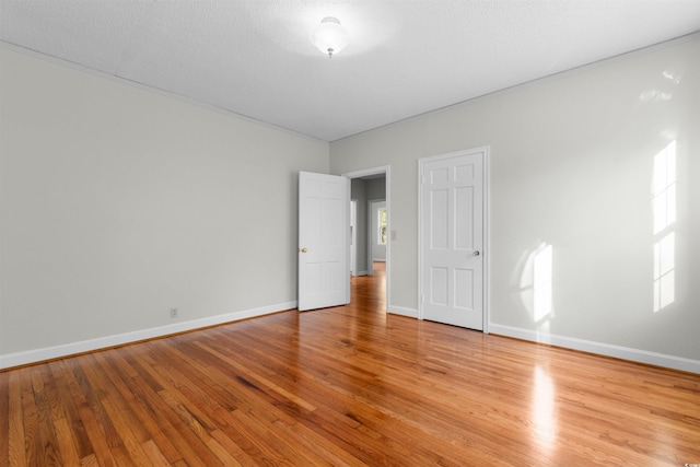 empty room featuring a textured ceiling, light wood-type flooring, and baseboards