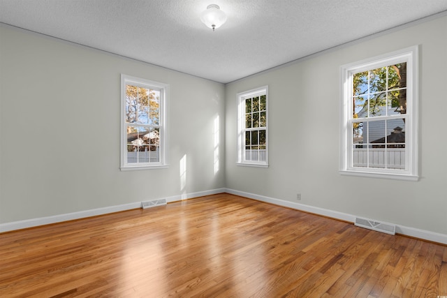 spare room featuring light wood-type flooring, visible vents, and a textured ceiling