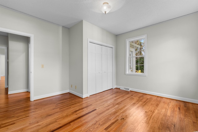 unfurnished bedroom with a closet, baseboards, a textured ceiling, and light wood finished floors