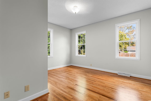 unfurnished room featuring baseboards, a textured ceiling, visible vents, and light wood-style floors