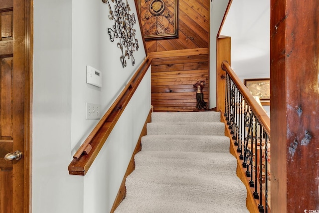 staircase with wooden walls, a towering ceiling, and carpet floors