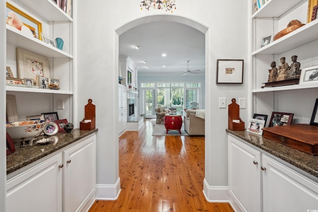 bar featuring white cabinets, light hardwood / wood-style floors, dark stone counters, and ceiling fan