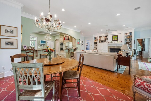 dining room featuring hardwood / wood-style floors, ceiling fan with notable chandelier, built in shelves, and crown molding