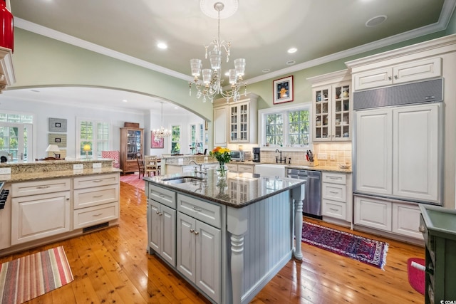 kitchen featuring white cabinets, light hardwood / wood-style flooring, stainless steel dishwasher, and decorative light fixtures