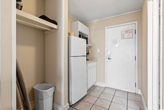 kitchen featuring light tile patterned flooring, built in microwave, a textured ceiling, white cabinets, and white refrigerator