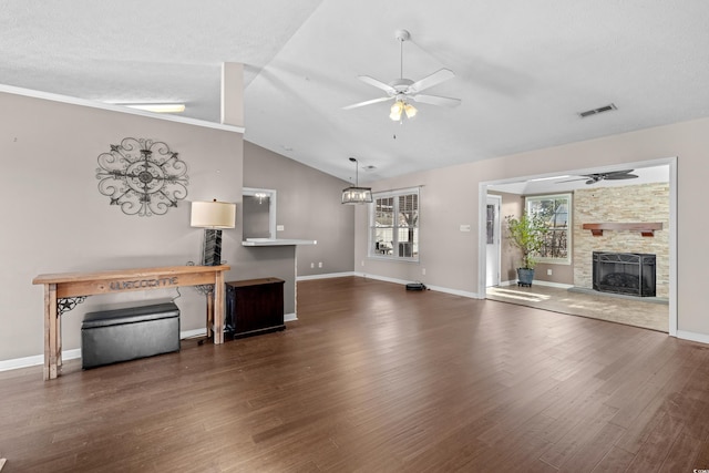 unfurnished living room with lofted ceiling, ceiling fan, a stone fireplace, wood finished floors, and baseboards